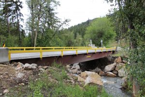 an angle of the surespan bridge rental with mountains and trees in the background. Rocks and dirt can be seen in the foreground.