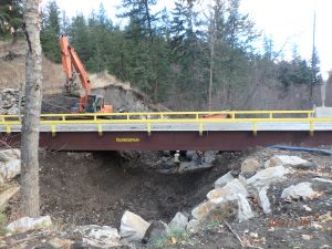 an angle of the surespan bridge rental with mountains and trees in the background. Rocks and dirt can be seen in the foreground.